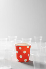 Eco friendly red paper cup surrounded by plastic cups on a gray table. Plastic-free concept, biodegradable tableware, recyclable. Space for text
