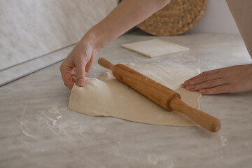 The girl rolls out the dough with a wooden rope on the table. Selectiv focus
