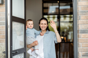 Housewife with newborn baby staying in front of entrance and waving goodbye to husband. Family...