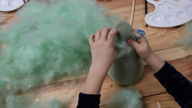 POV toddler girl fingers stuffing soft sintepon inside handicraft felt toy. Green cotton sintepon hollow PP cotton filling material for making stuffed toys. Kids sensory activity for fine motor skills
