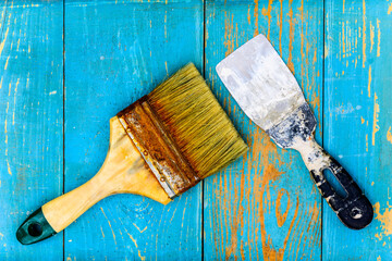 Old paint brush and spatula on old wooden table covered with blue paint. View from above
