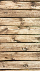 A wooden pier. The floor is made of wooden boards. Natural material used in construction work. There are a few nails heads visible. The wooden boards are a bit used up. Natural colors and patterns