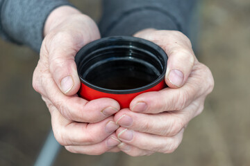 a mug of hot tea in women's hands at a picnic