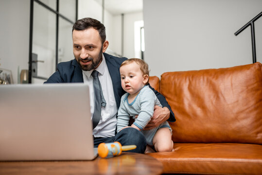 Young Businessman Dad Working On A Laptop At Home While Taking Care Of His Newborn Son. Multitasking And Babysitter.