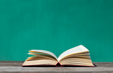 An open book lies on a gray wooden table on a turquoise background