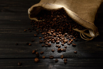 Coffee beans spill out of the burlap bag on a black wooden table.