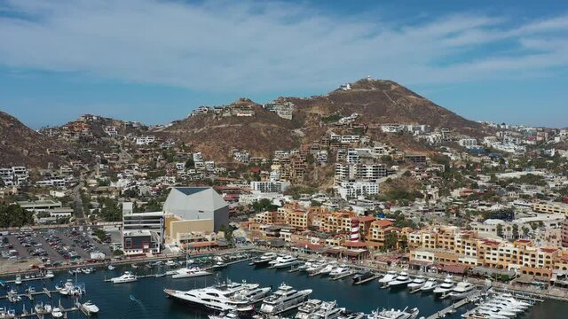 Aerial panoramic view of Cabo San Lucas, México, the drone slowly descending over the Marina with a blue and cloudy sky as background.