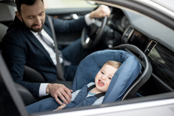 Father tend a child while driving at work with baby sitting in modern car seat. Child new born traveling safety on the road. Safe way to travel fastened seat belts in a vehicle with young kids. 