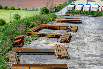 Long and thick, rust-covered steel bars stacked outside on a gravel square, viewed from above.