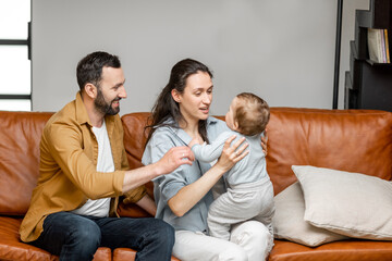 Happy father, mother and little son are playing on sofa in living room. Child care and parenting. 