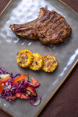 Beef steak with corn and salad on a gray plate