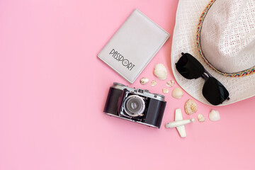 Female straw white hat, passport, black sunglasses, old vintage retro camera, toy mini plane and seashells isolated on a light color pink background. Top view, flat lay. Summer vacation travel concept