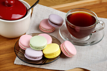 Multicolored macaroons and a cup of tea on a wooden tray. Morning tea and sweets.