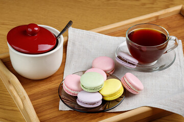 Multicolored macaroons and a cup of tea on a wooden tray. Morning tea and sweets.