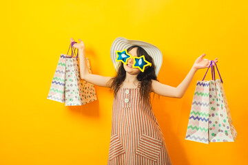 Attractive cute kid girl in summer clothes,beach hat and big sun glasses is holding shopping bags,...