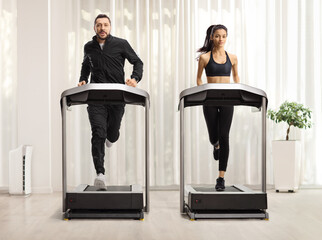 Young man and woman running on treadmills with curtain in the background