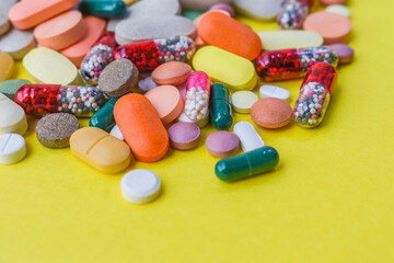 Close up of various medicine tablets, capsules and pills different colors on yellow background.