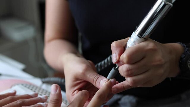 Anonymous master polishing nails of female customer with electric file