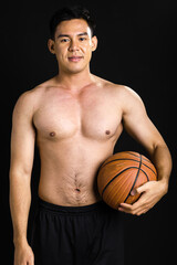 Asian strong healthy handsome muscular sportive man with shirtless, holding basketball, smiling with confidence, posing, looking at camera with confidence, standing on isolated black background.