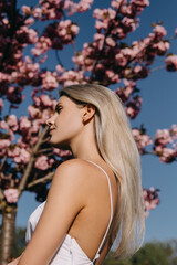 Portrait of a young woman with long blonde hair outdoors, in a park, on cherry tree in bloom background.