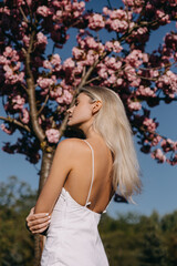 Young woman with long blonde hair outdoors, in a park, on cherry tree in bloom background.