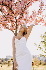 Young woman with long blonde hair outdoors, in a park, on cherry tree in bloom background.