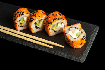 Traditional sushi and chopsticks. Philadelphia with salmon, avocado and cheese. Japanese cuisine on black background