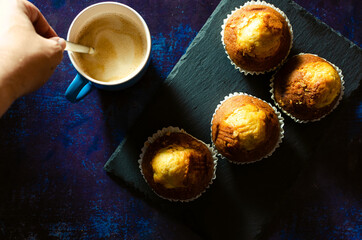Stirring breakfast coffee with muffins on a slate plate on a rusty blue background. Dark food