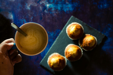 Hand picking up breakfast coffee with muffins on slate plate on rusty blue background. Dark food. Selective focus