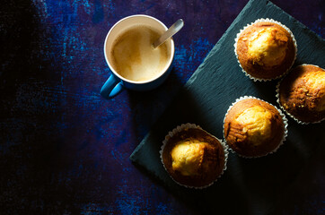 Breakfast of coffee with muffins on a slate plate on a rusty blue background. Dark food