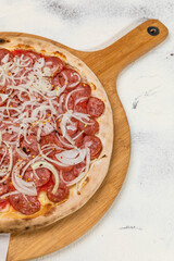 Pepperoni Sausage Pizza with Onion Homemade Artesanale Close Up Detail on a Round Wooden Plate with Flour Background Table