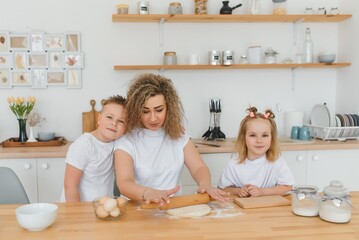 Obraz na płótnie Canvas An attractive smiling family of mother, and two children, boy, girl, son, daughter cookies in a kitchen at home