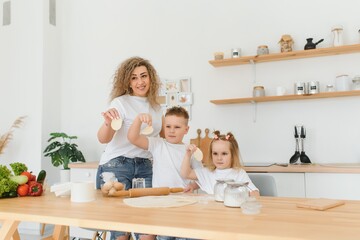 Happy young mother with cute little preschooler kids have fun making dough baking pie or pastry in modern kitchen together, overjoyed mother teach small children doing bakery cooking at home