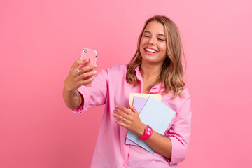 blond pretty woman in pink shirt smiling holding holding notebooks and using smartphone