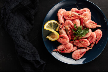 shrimp on a blue plate with lemon on a black textured background top view
