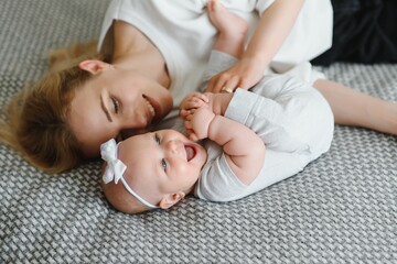 Young tender happy mother hugging her newborn baby smiling sitting on bed in morning.