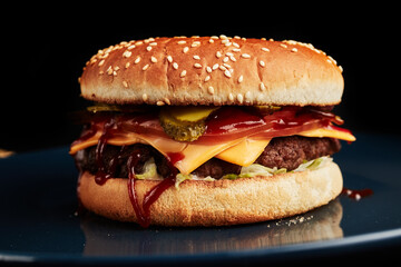 burger on a blue plate on a black background with a golden twig overhead side view