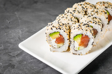appetizing california sushi roll with cheese avocado cucumber and salmon in sesame seeds on a black...