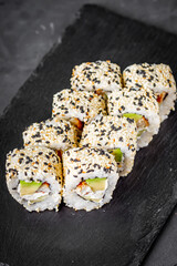 appetizing sushi roll california with eel avocado cucumber and sesame seeds on a black stone plate