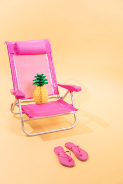 Pink beach chair with a paper pineapple on top and pink flip flops