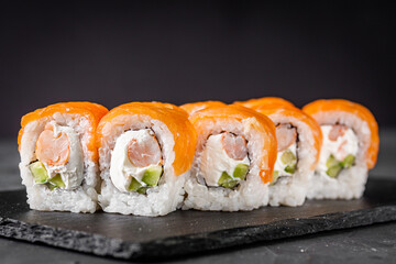 appetizing sushi roll philadelphia with shrimp cheese cucumber and salmon on a black stone plate