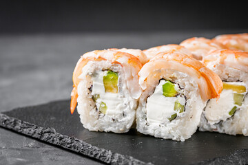 appetizing sushi roll philadelphia with avocado cheese cucumber and shrimp on a black stone plate