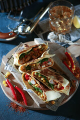 Mexican cuisine. Tortilla with vegetables, herbs, corn, meat, chili pepper and spices. Chimichanga with a glass of whiskey, gun, newspaper and lime on an old wooden board. Background image, copy space
