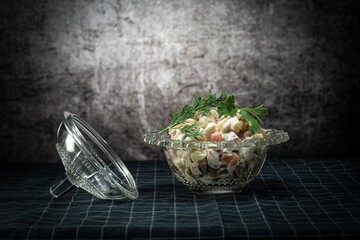 Olivier salad, in a glass salad bowl, on a rag napkin, on a background with a stain