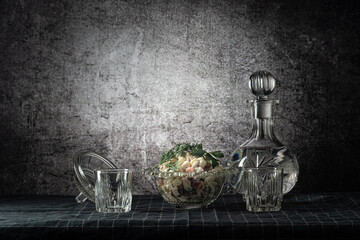 A decanter and two glasses, with a strong drink, and an olivier salad, on a dark tablecloth