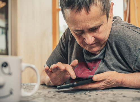 Elderly Woman Typing Intently On Her Smartphone. Woman With Mental And Physical Disability Operating Her Smartphone. Head Close To Device Due To Visual Impairment