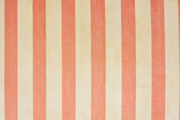 A fragment of the upholstery of an old mattress with red and white transverse stripes. The fabric has aged, there are traces of dirt and liquid drips on it. Background. Texture.
