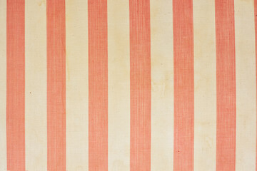 A fragment of the upholstery of an old mattress with red and white transverse stripes. The fabric has aged, there are traces of dirt and liquid drips on it. Background. Texture.