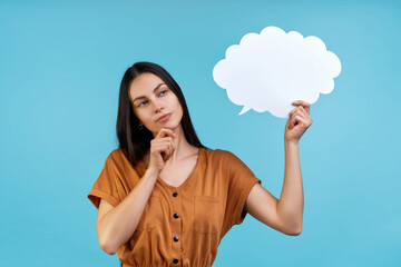 Studio shot of beautiful confident young woman holding blank paper speech cloud in hand and holding finger on chin, thinking over new idea