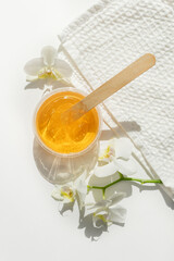 Sugar paste or wax honey in a transparent jar and white orchid on a white background. Sugaring....